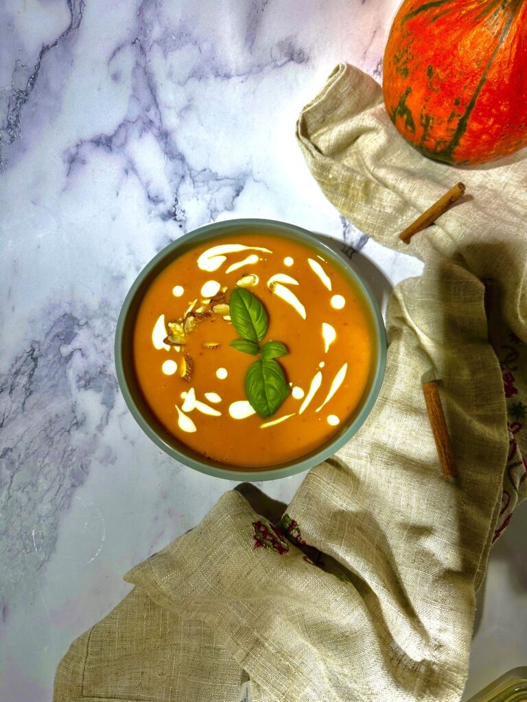 A bowl of anti inflammatory Hokkaido pumpkin soup, with a creamy coconut milk texture, garnished with freshly black pepper and roasted almond. Healthy winter food.