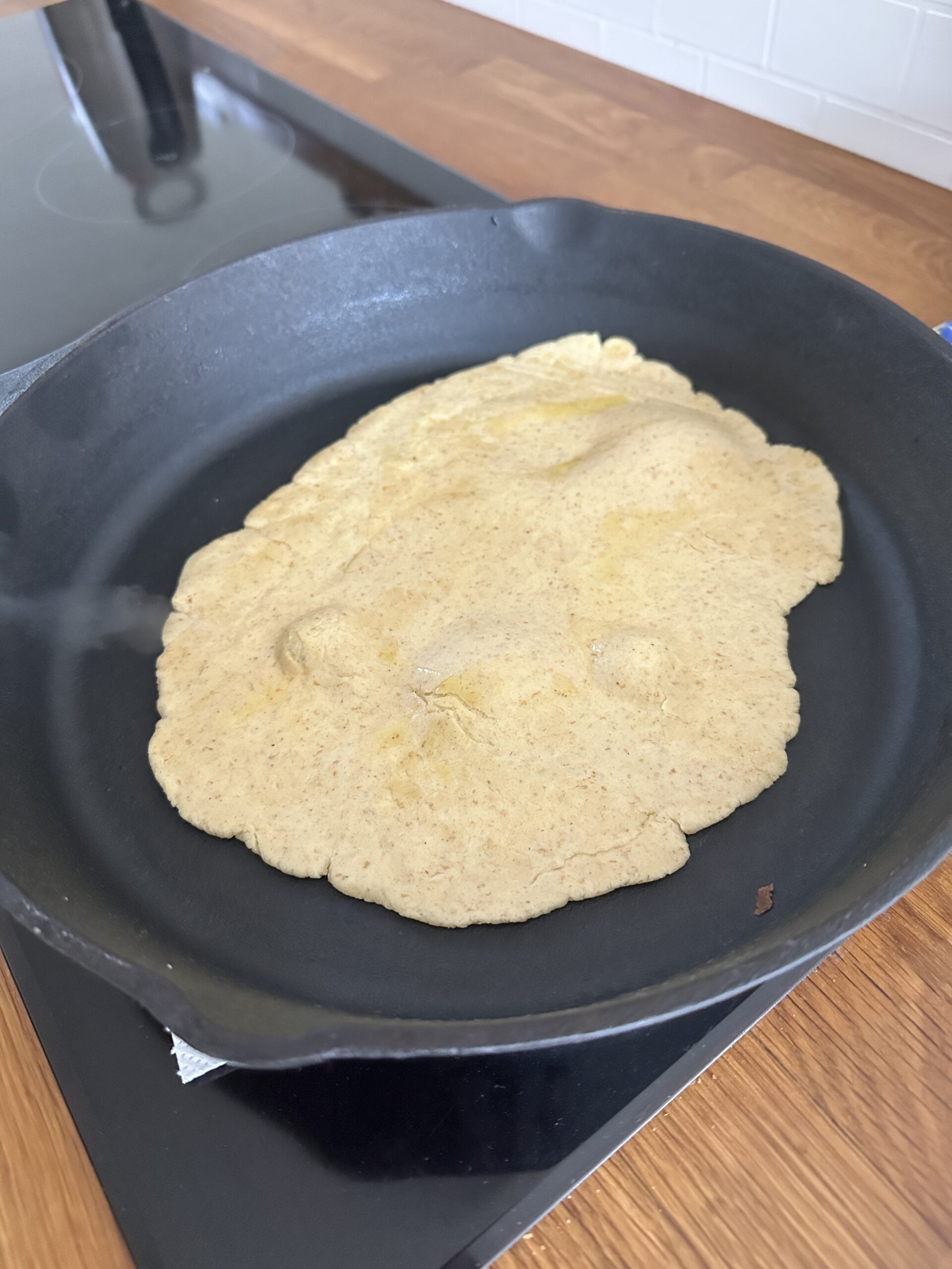 Sourdough tortilla cooking in a skillet with golden brown spots forming