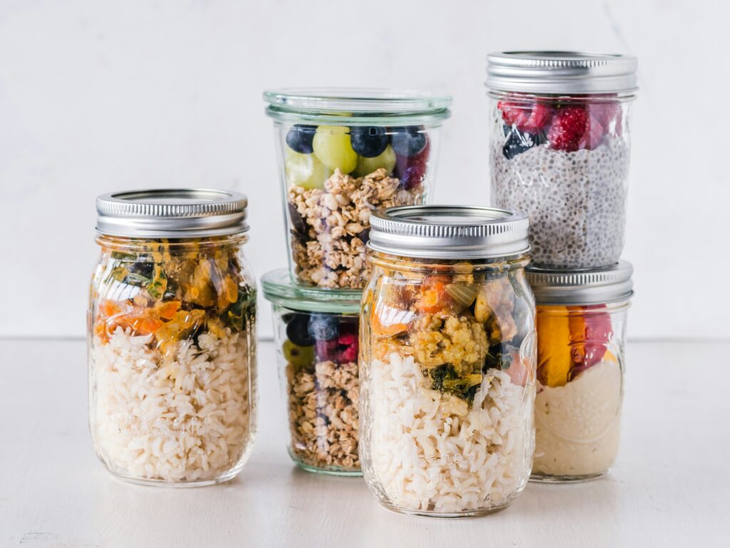 Glass meal prep jars filled with rice, granola, fruit, chia pudding, and layered make-ahead meals on a bright white background.